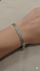 Silver bracelet on a wrist against a neutral background