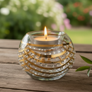 Decorative glass candle holder with a lit candle on a wooden surface outdoors.