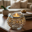 Decorative glass candle holder with a lit candle on a wooden table in a living room setting.