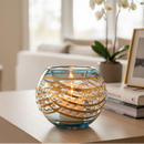 Decorative candle holder with gold ribbons on a table in a bright room.