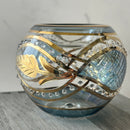 A hand-blown glass tea light holder with a swirl pattern in blue and gold colors, featuring a base and a lid with gold accents.