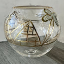 A hand-blown glass tea light holder with a geometric pattern, featuring a mix of clear and gold colors, displayed on a wooden surface.
