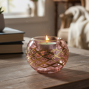 Pink glass candle holder with a lit candle on a wooden surface