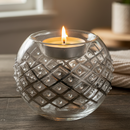 Glass candle holder with a lit candle on a wooden surface