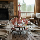 Dining table set with pink glassware and a decorative lamp in a rustic setting.