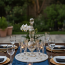 Dining table set with glasses, plates, and a candle under string lights outdoors.