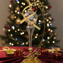Decorative Christmas ornament with gold and clear design on a red surface with a blurred Christmas tree in the background.