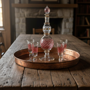 Decorative glass decanter and tumblers on a wooden tray with a stone fireplace in the background.