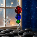 Decorative glass ornament with red, blue, and green beads hanging against a snowy window background.
