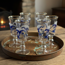 Set of six decorative glass goblets on a metal tray with a fireplace in the background