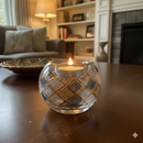 Candle in a decorative glass holder on a wooden table with a cozy living room background.
