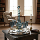 Decorative blue glass set on a silver tray in a room with bookshelves and windows.