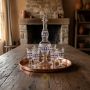 Decorative glass set with a large bottle and small glasses on a wooden tray in a rustic room.