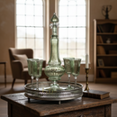 Green glass decanter and goblets on a silver tray with stained glass windows in the background.