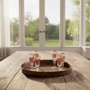 Set of six small glasses with red patterns on a wooden tray in a bright room with large windows.