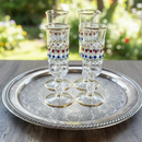 Set of four decorative glasses on a silver tray with a blurred garden background