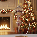 Decorative glass ornament on a stand with a festive background including a Christmas tree and fireplace.