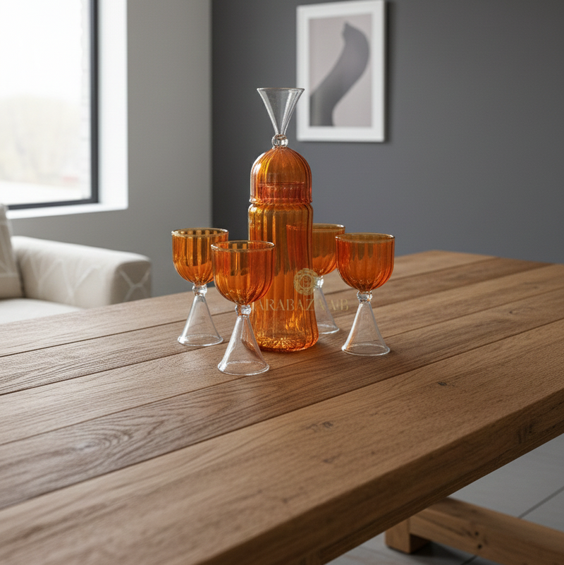 Set of orange glassware on a wooden table with a gray wall and framed picture in the background.