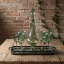 Green glass decanter and goblets on a wooden table with a brick wall background