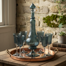 Decorative blue glass set with a tall central piece and multiple glasses on a wooden tray against a stone wall.