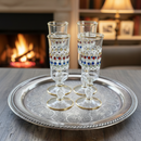 Four decorative glasses with colored dots on a silver tray in front of a fireplace.