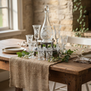 Decorative table setting with glasses, a decanter, and a burlap runner on a wooden table.