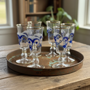 Set of six small glasses with blue patterns on a metal tray, placed on a wooden surface.
