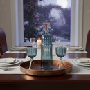 Dining table set with blue glassware and a candle, window in the background showing outdoor scene.