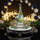 Decorative glass set with carafe and cups on a marble stand with flowers and lights in the background.