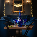 Decorative blue vase and glasses on a tray with a blurred background of a room with lights.