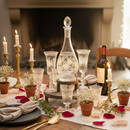 Dining table set for a meal with wine glasses, decanter, and candles in front of a fireplace.