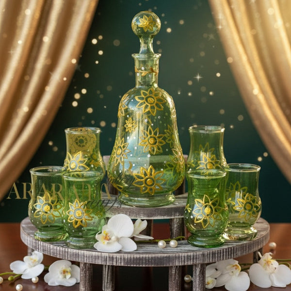 Green glass decanter and glasses with floral designs on a wooden stand, surrounded by white flowers.