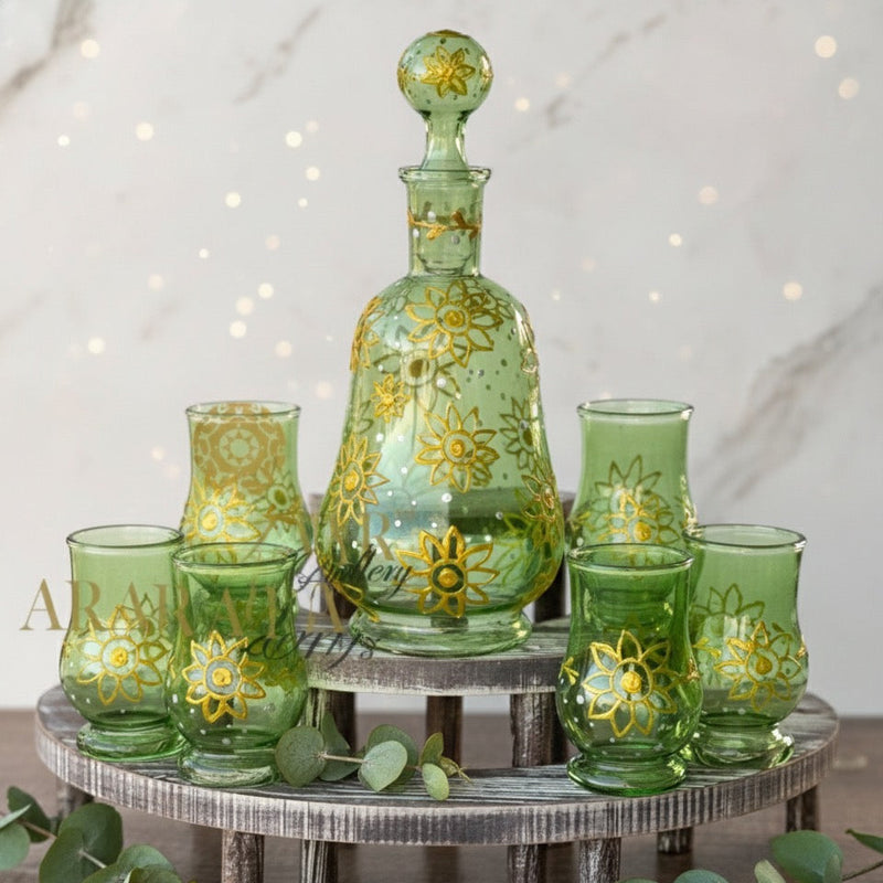 Green glass decanter and tumblers with floral patterns on a wooden stand.