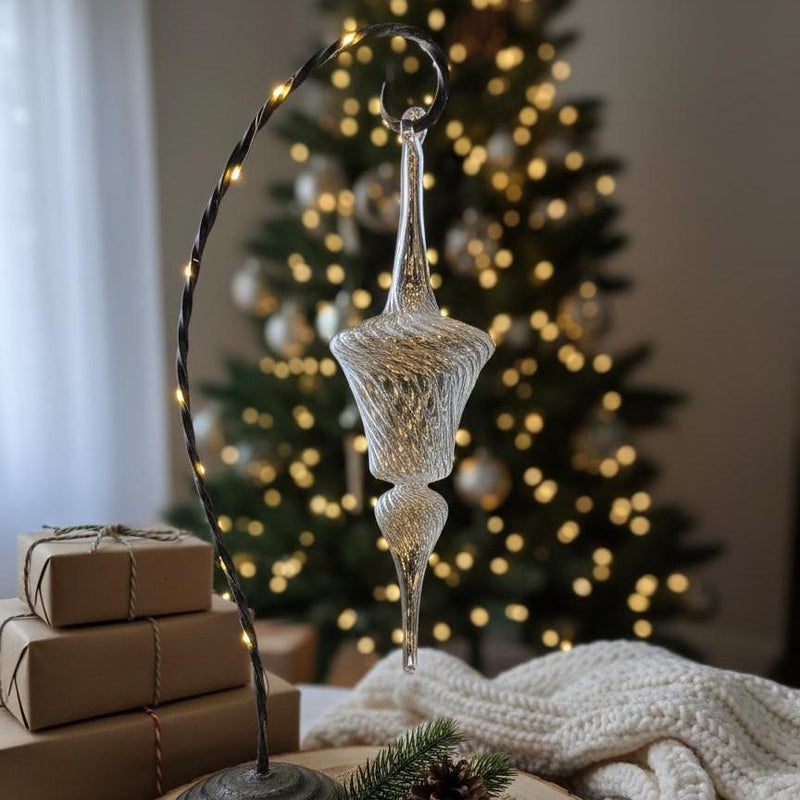 Decorative glass ornament on a stand with a Christmas tree and presents in the background