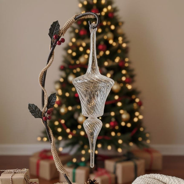 Decorative glass ornament with a branch in front of a Christmas tree and presents.