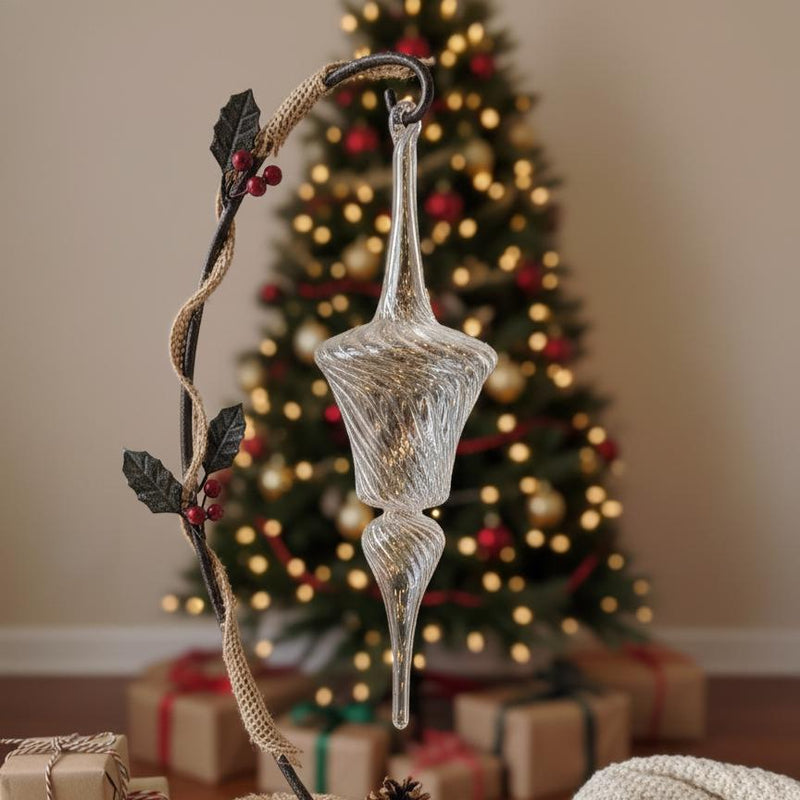 Decorative glass ornament with a branch in front of a Christmas tree and presents.