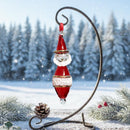 Decorative Christmas ornament of Santa Claus on a stand with a snowy landscape background.
