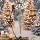 Decorative Christmas ornament with holly leaves and berries against a festive background with lights and candles.