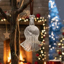 Clear glass angel ornament hanging on a tree branch with festive lights in the background