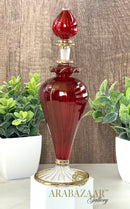 Decorative red glass bottle with gold accents on a white pedestal, against a wooden background with plants.
