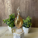 Decorative glass bottle with gold accents on a marble surface with plants and 'ARABAZAAR Gallery' branding.