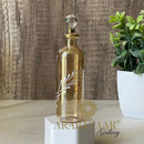 Decorative glass bottle with engraved design on a wooden surface with a plant in the background