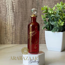 Red decorative bottle with gold accents on a white stand, next to a plant against a wooden background, with 'ARABAZAAR Gallery' branding.