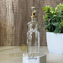 Decorative glass bottle with intricate designs on a wooden surface with a plant in the background.