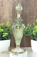 Decorative glass bottle with gold accents on a wooden surface with plants in the background