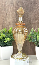 Decorative glass bottle with gold accents on a wooden surface with plants in the background