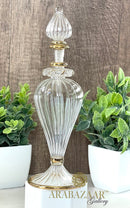 Decorative glass bottle with gold accents on a wooden surface with plants in the background