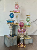 A collection of handblown glass oil burners with unique crystal designs and 14K gold liner details, displayed in various colors such as purple, green, pink, and blue.